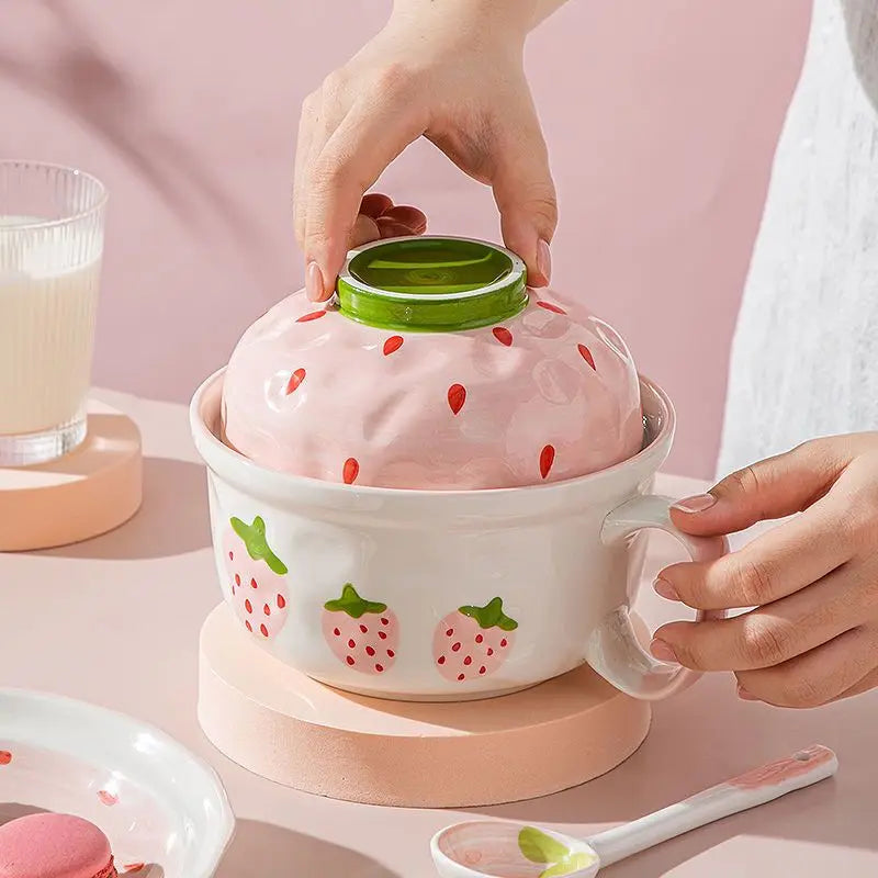 Person holding a strawberry-patterned kawaii bowls with a matching lid on a pink background