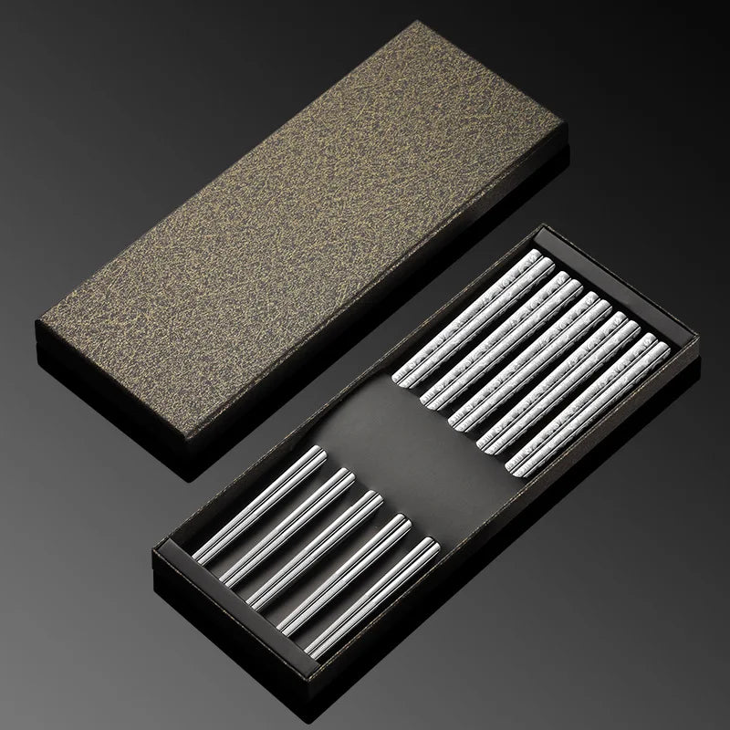Set of metal kawaii chopsticks in a black box with a textured brown block on a dark background