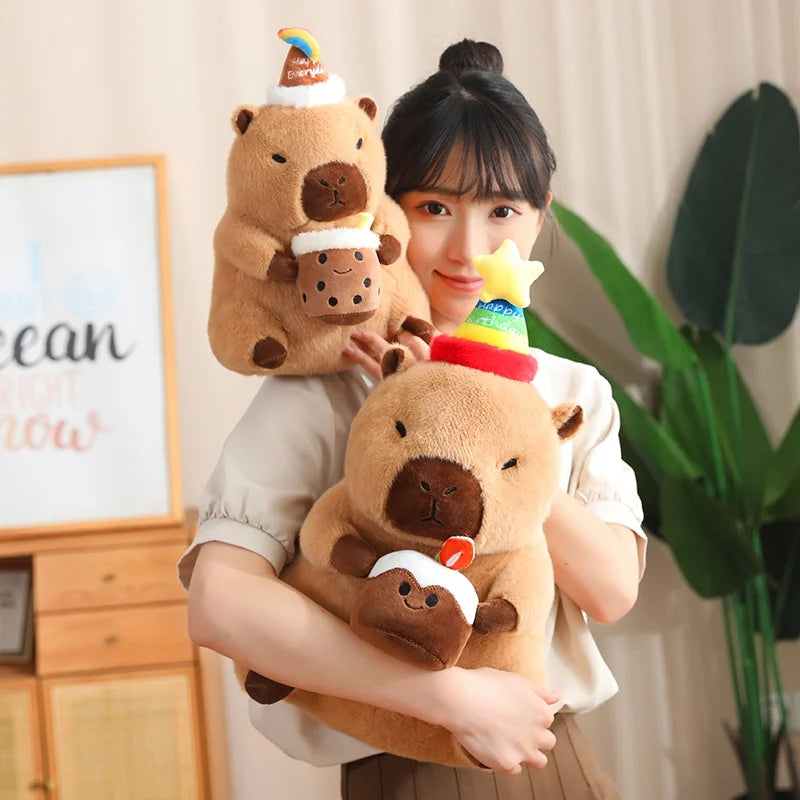 Person holding a capybara plush toys with decorative hats in a home setting