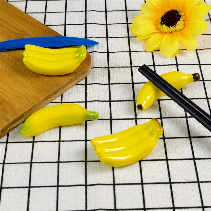 Yellow banana-shaped kawaii chopstick holders on a checkered tablecloth with a wooden cutting board and black chopsticks.