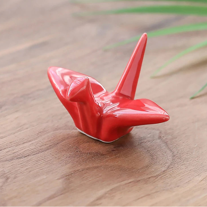 Red ceramic bird kawaii chopstick holders on a wooden surface with grass in the background