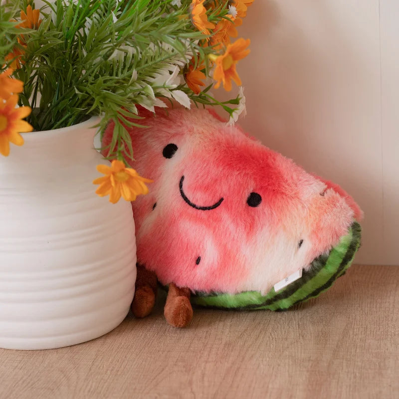 Kawaii plush watermelon toy with a smiling face next to a potted plant on a wooden surface.