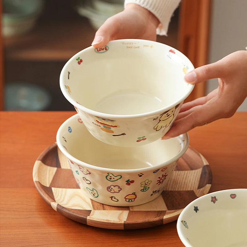 Two stacked ceramic kawaii ramen bowls with cartoon designs on a wooden tray.