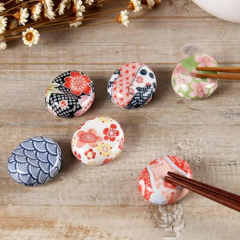 Set of decorative ceramic kawaii chopstick holders with floral patterns on a wooden surface.