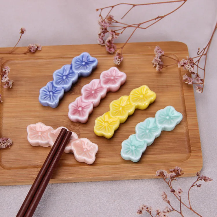 Colorful flower-shaped kawaii chopstick holders on a wooden board with chopsticks and dried flowers.