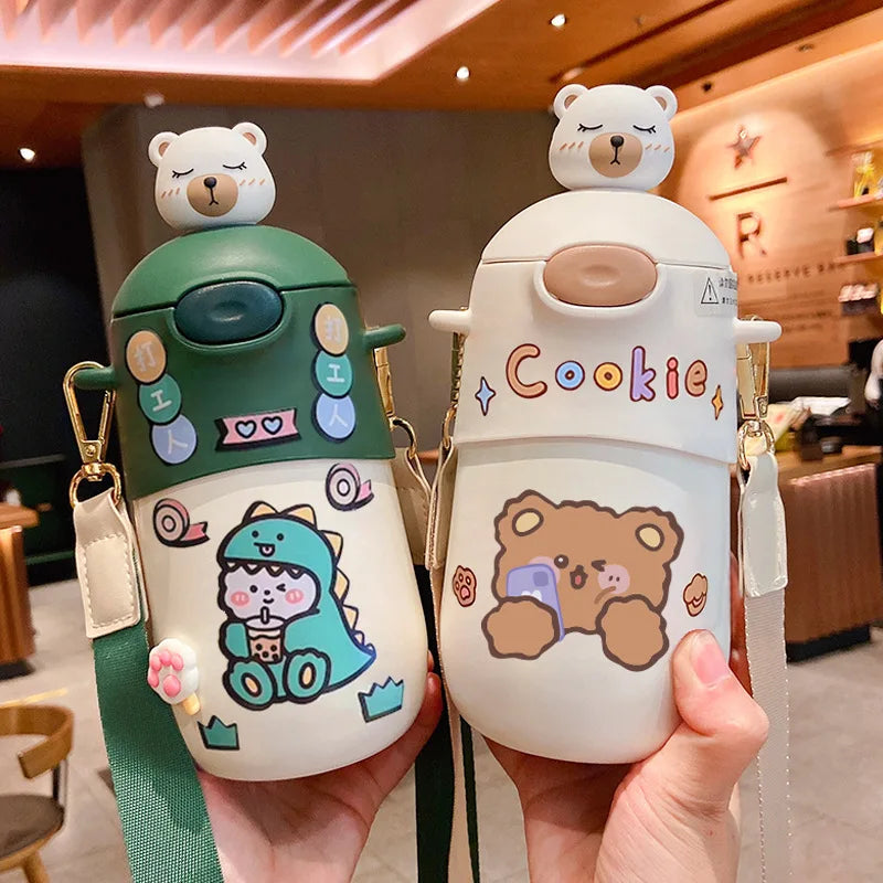 Two cute cartoon-style kawaii water bottles held in a hand, one green and one white with a bear design, in an indoor setting.