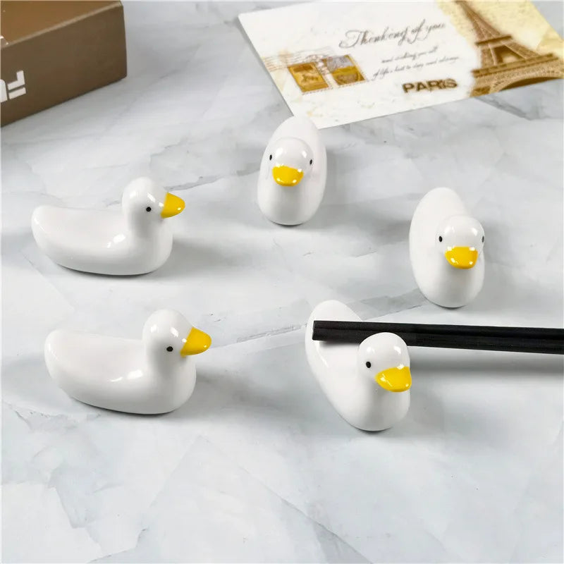 Set of white duck-shaped kawaii chopstick holders on a marble surface with a card in the background.