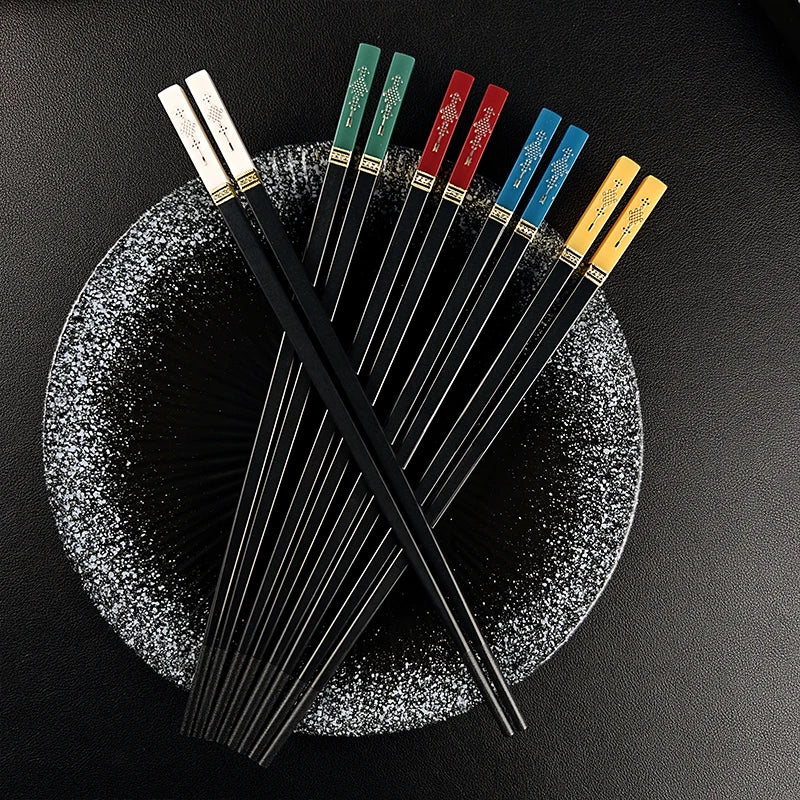 Set of black kawaii chopsticks with colored handles on a textured black plate.