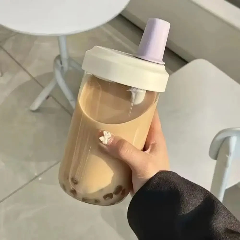 Hand holding a transparent kawaii cup with a white lid and purple top, filled with a brown liquid.