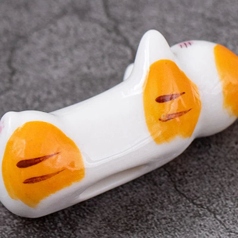 White and orange cat-shaped kawaii chopstick holders on a gray surface