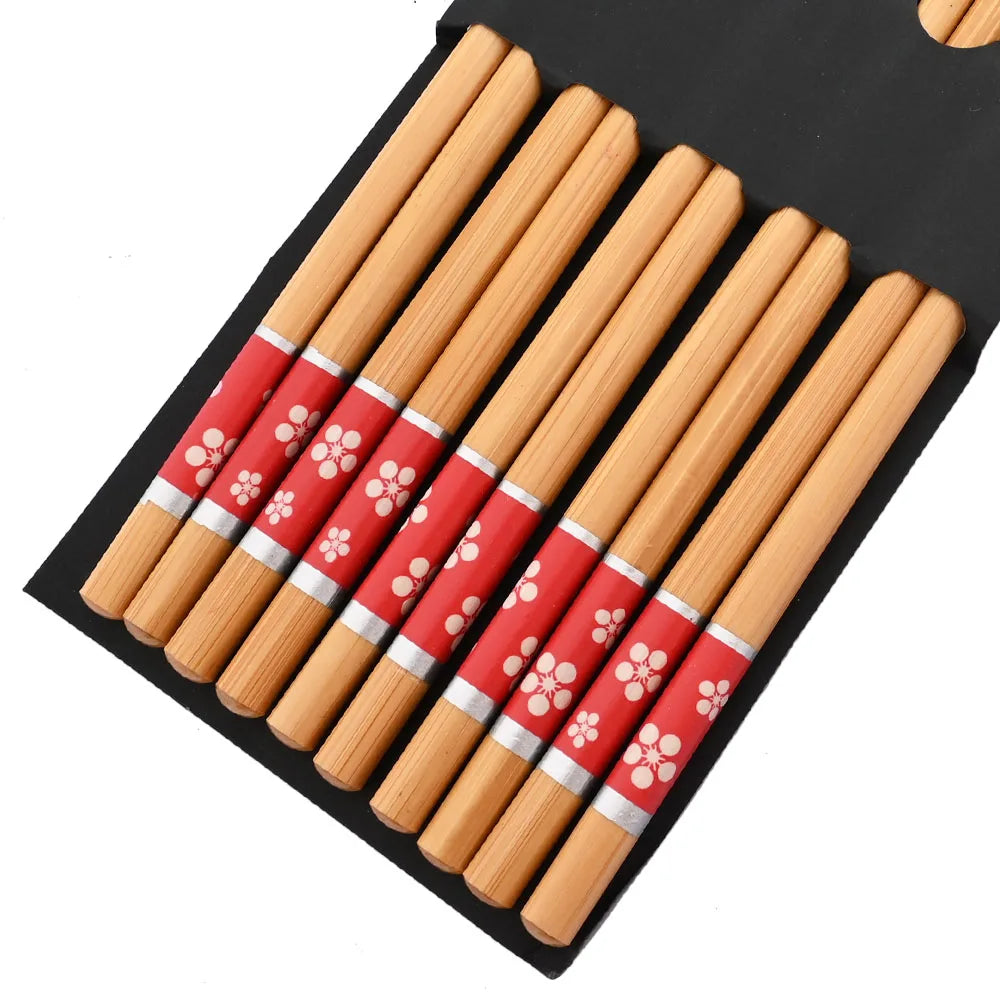 Set of wooden kawaii chopsticks with red handles featuring white floral patterns, on a black mat.
