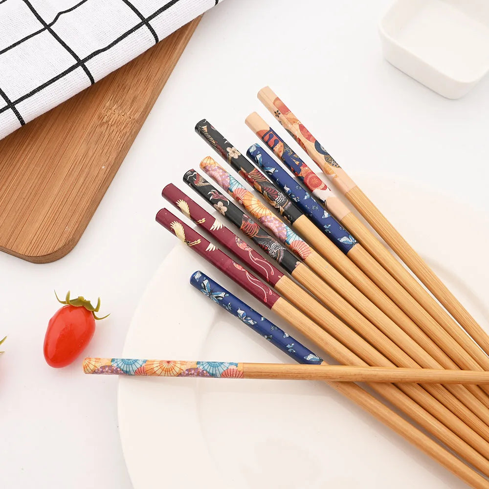 Set of decorative kawaii chopsticks on a white surface with a wooden cutting board and small red tomato.