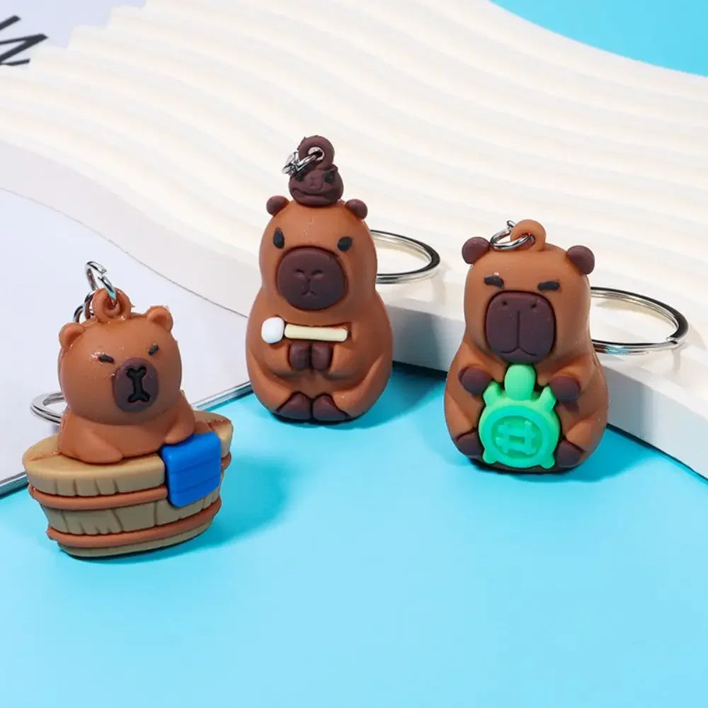 Three kawaii bear-shaped keychains on a light blue surface with a white book in the background.