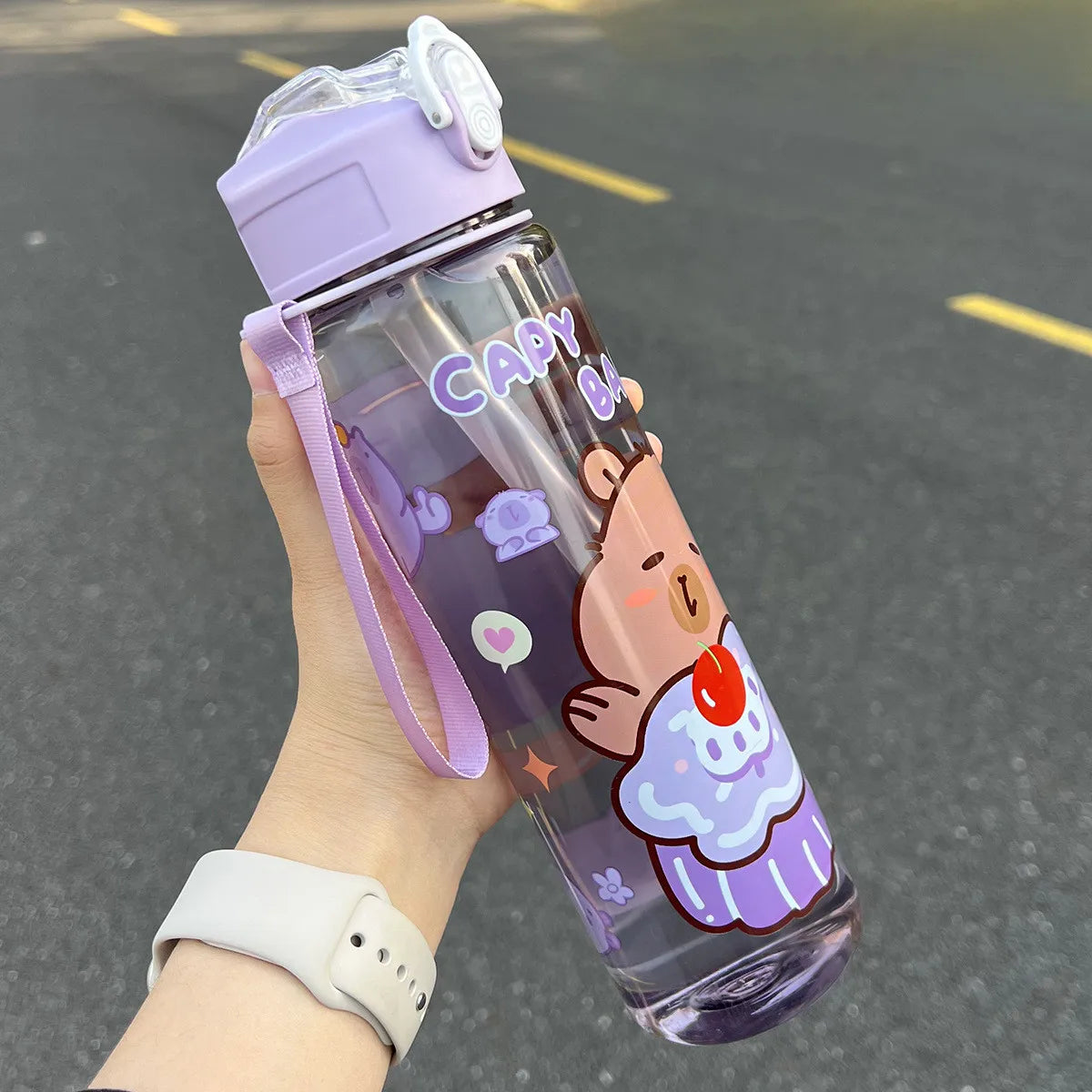 Hand holding a purple kawaii-themed water bottle on a dark surface