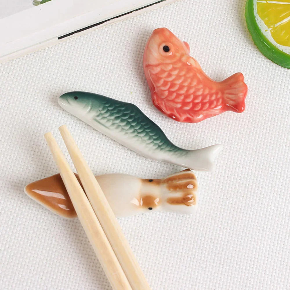 Three fish-shaped ceramic kawaii chopstick holders on a white surface with chopsticks.