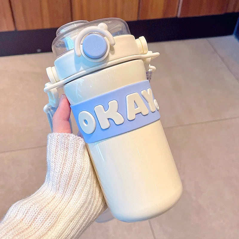 White and blue kawaii water bottle with 'OKAY' strap held by a person wearing a white knit sleeve.