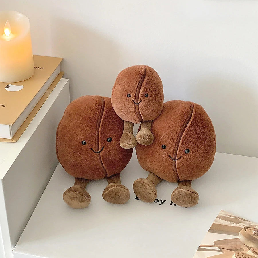 Three brown kawaii plush toys resembling walnuts on a white surface with a candle and book in the background.