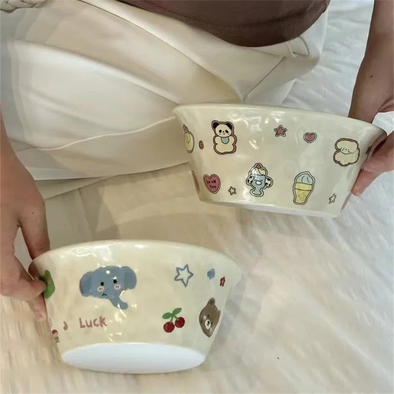 Two ceramic kawaii ramen bowls with cartoon designs held by a person on a light-colored surface.