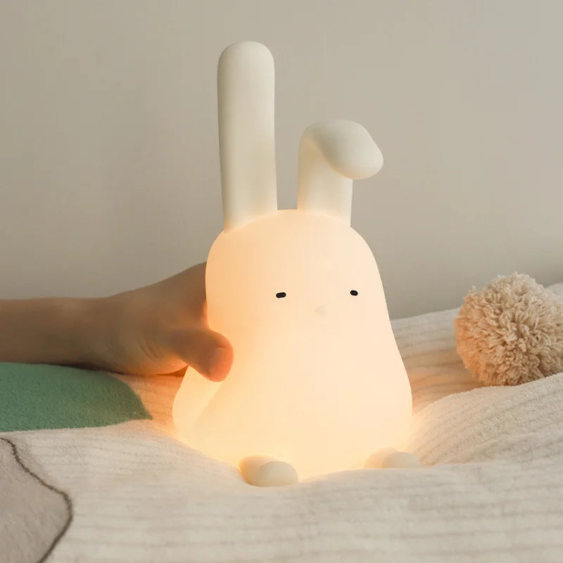 Cute rabbit-shaped kawaii night light being held by a hand on a soft surface.