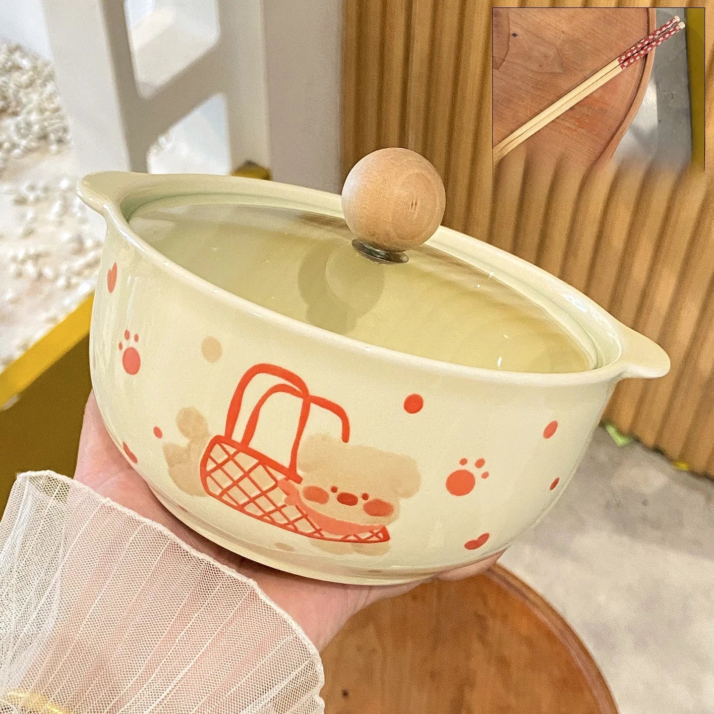 Ceramic kawaii ramen bowl with a wooden lid held by a person, featuring cute illustrations on a light background.