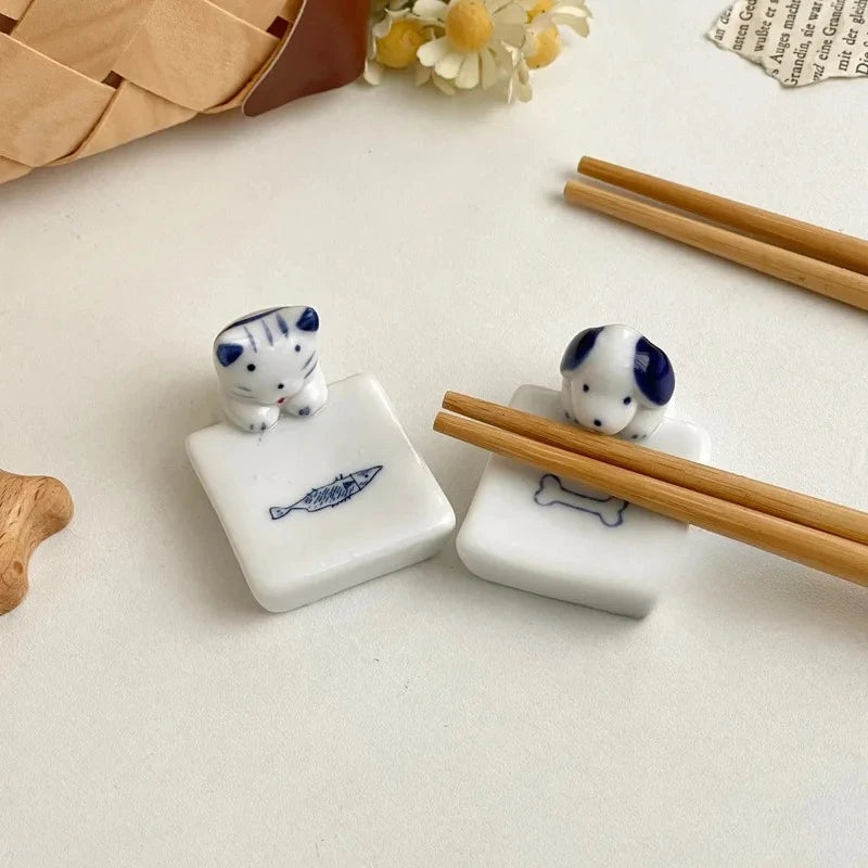 Two ceramic kawaii chopstick holders with cat designs on a light surface with wooden chopsticks.