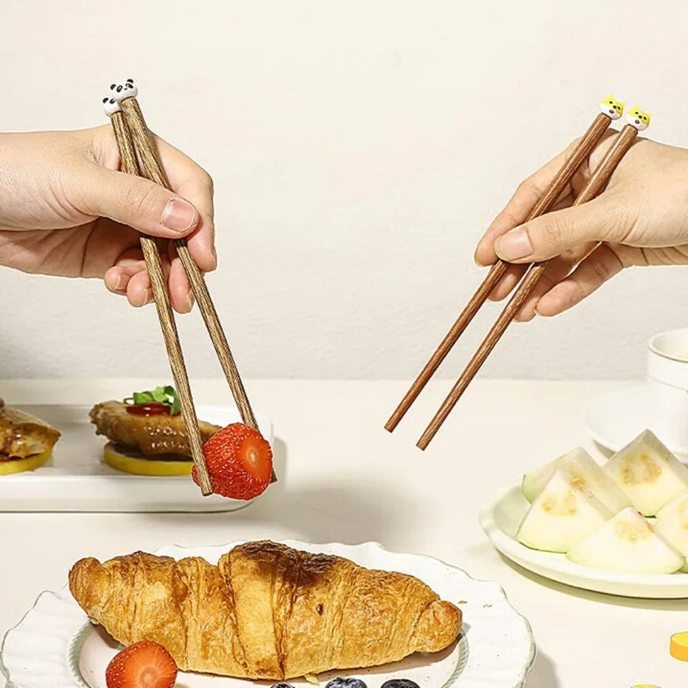 Two hands using kawaii chopsticks to pick up food from plates on a table.