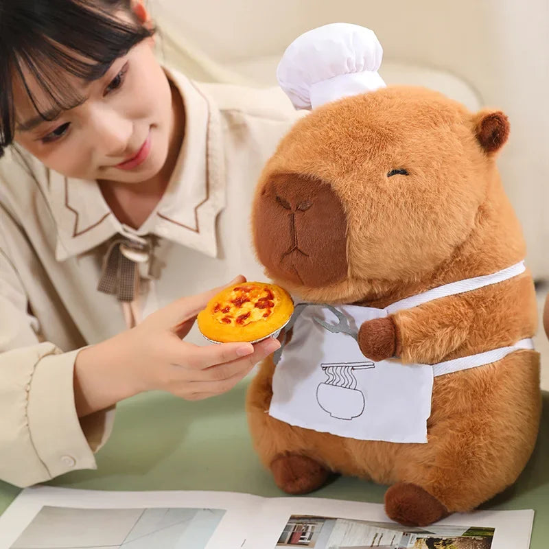 Person holding a small pizza next to a kawaii plush toy bear wearing a chef's hat and apron.