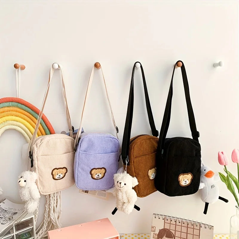 A group of four small tote bags with a bear design on the front, hanging up on the wall.