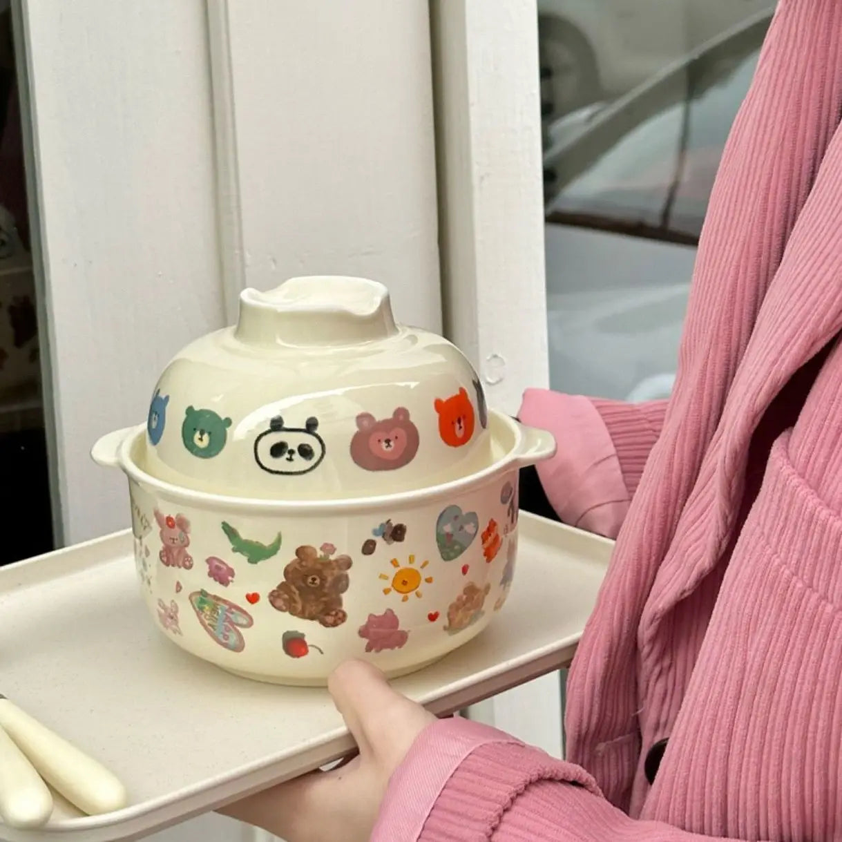 Ceramic kawaii bowl with cartoon designs held by a person wearing a pink sweater.