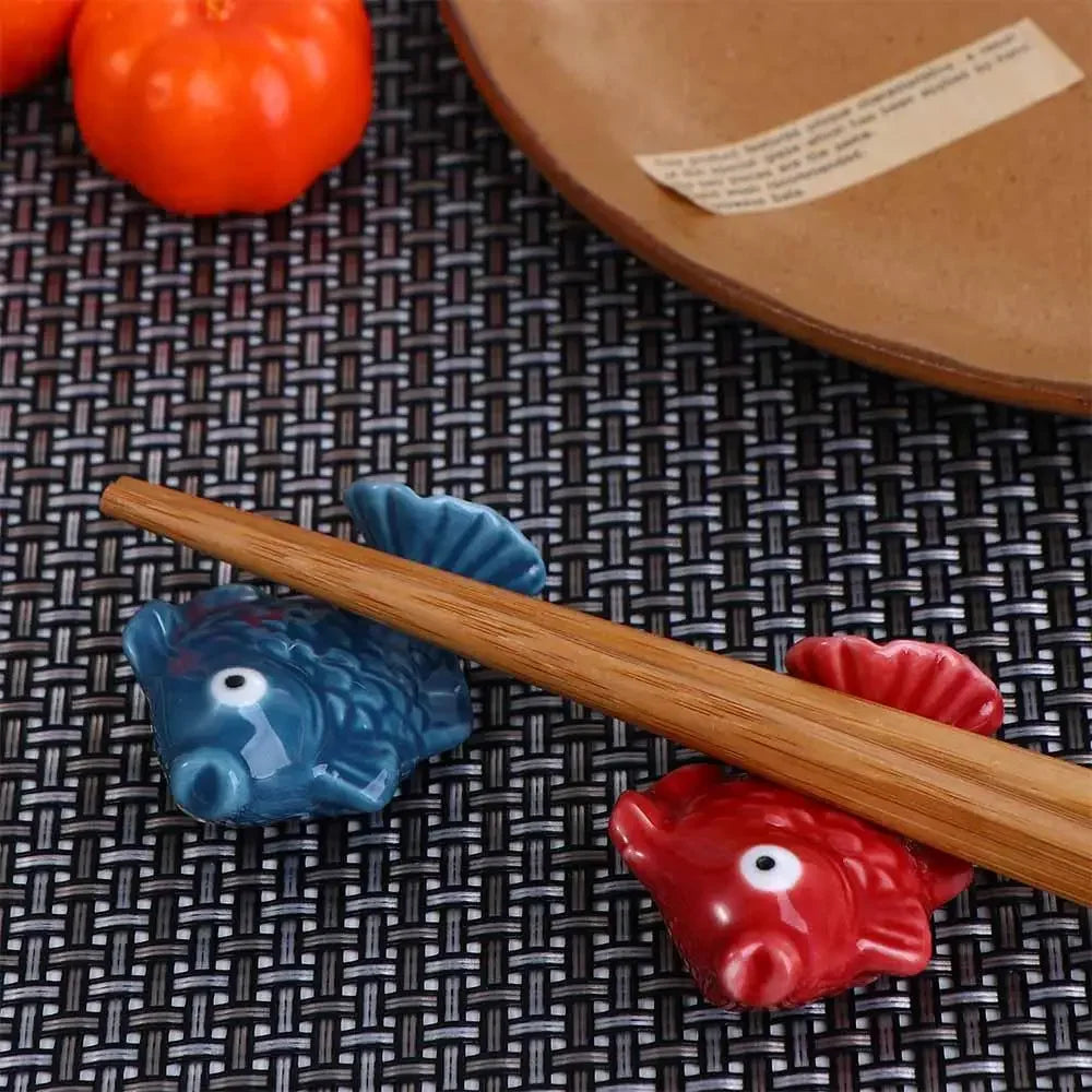 Two fish-shaped kawaii chopstick rests on a woven mat with a wooden plate in the background.