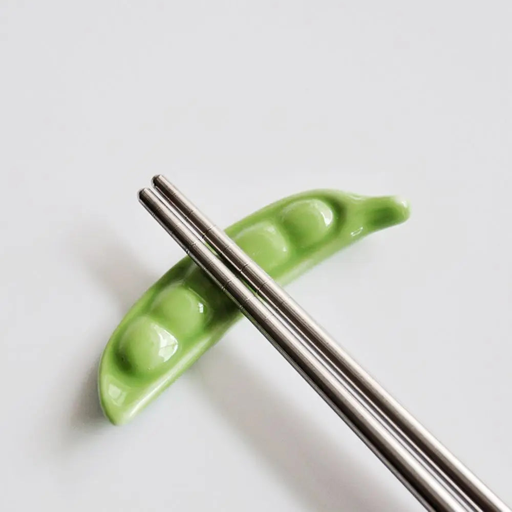 Green pea pods with metal kawaii chopstick holders on a white background