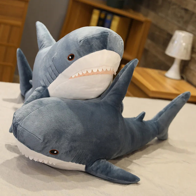 Large kawaii plush shark toy on a bed with a blurred room background