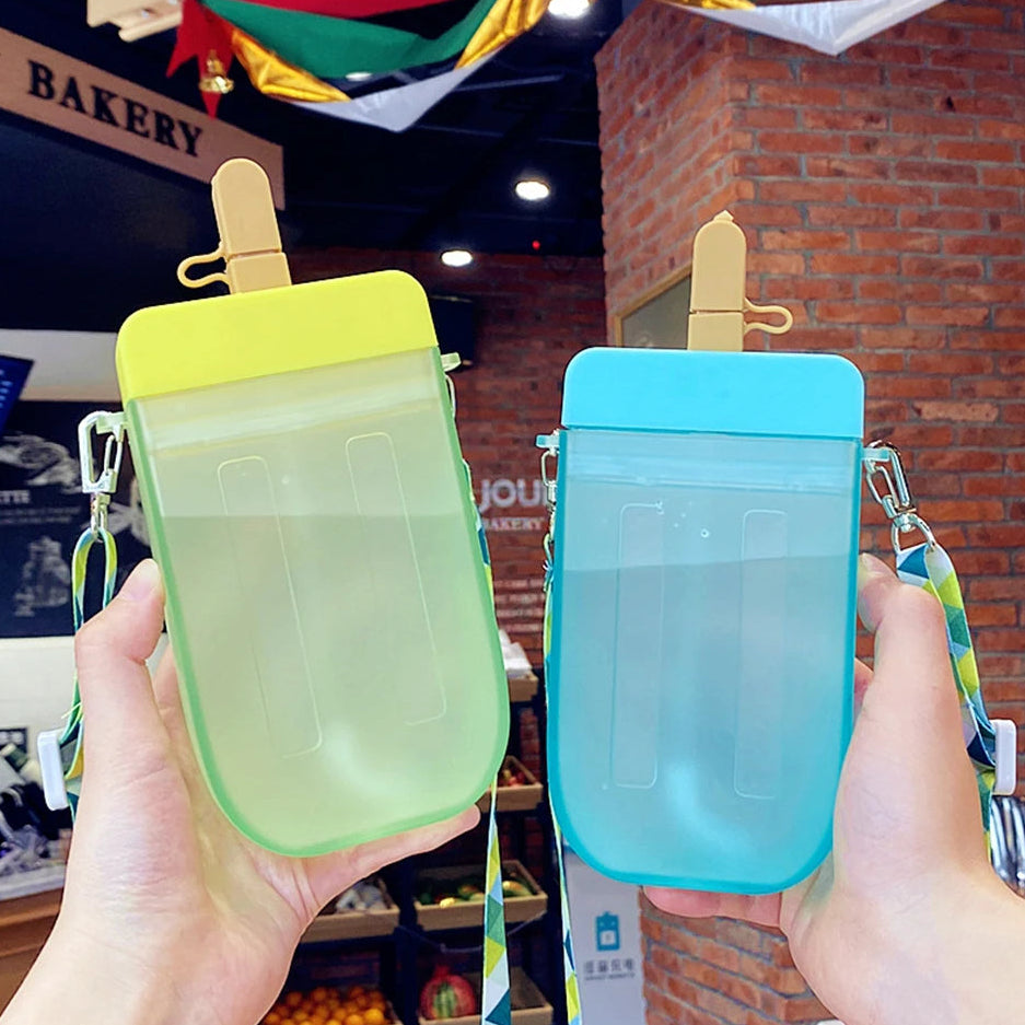 Two colorful kawaii water bottle shaped like popsicles held by hands in front of a bakery.