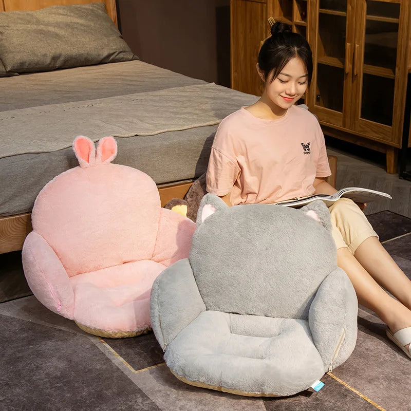 Woman sitting on a gray cat-shaped cushion next to a pink rabbit-shaped kawaii cushion in a bedroom.