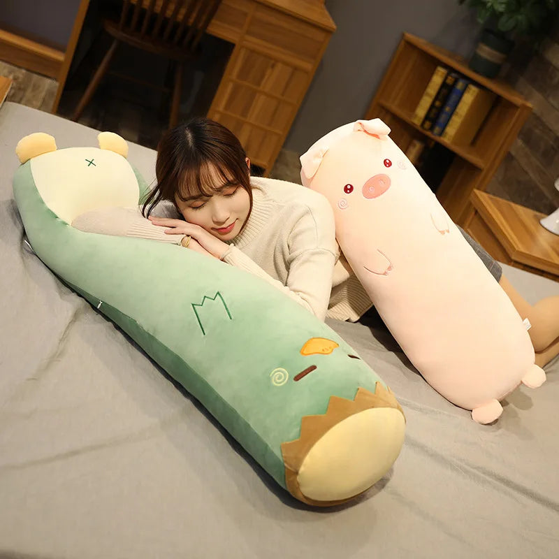 Woman lying on a bed with two large kawaii plush toys, one green and one pink, in a cozy room.