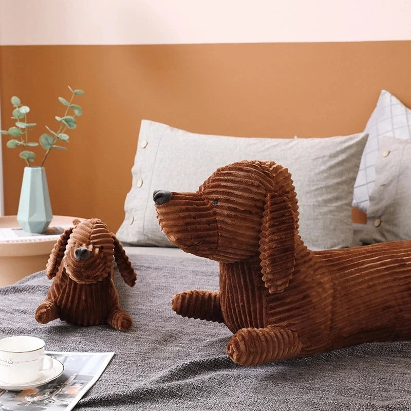 Two brown kawaii plush dachshunds on a bed with pillows and a plant in the background.
