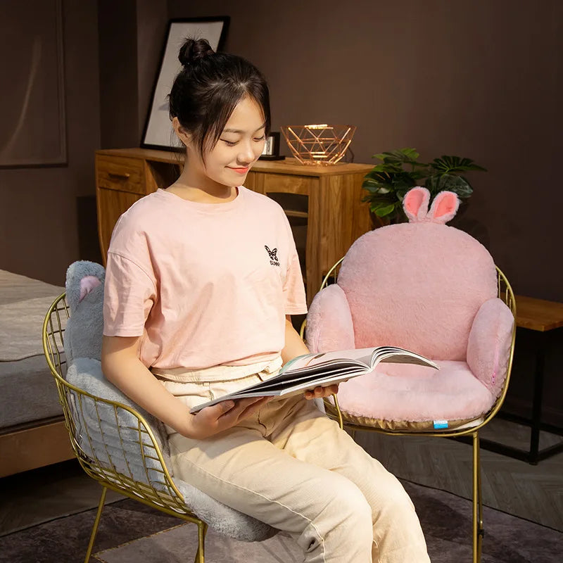 Woman sitting on a chair with a pink kawaii cushion and reading a book in a room.