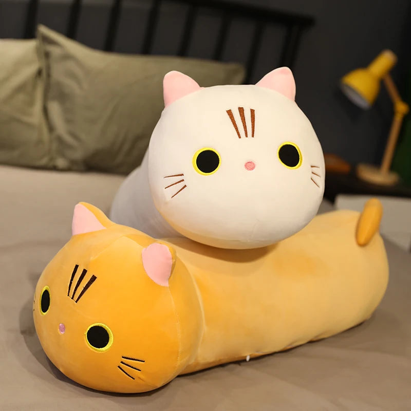 Two cat-shaped plush kawaii toys on a bed with a blurred background