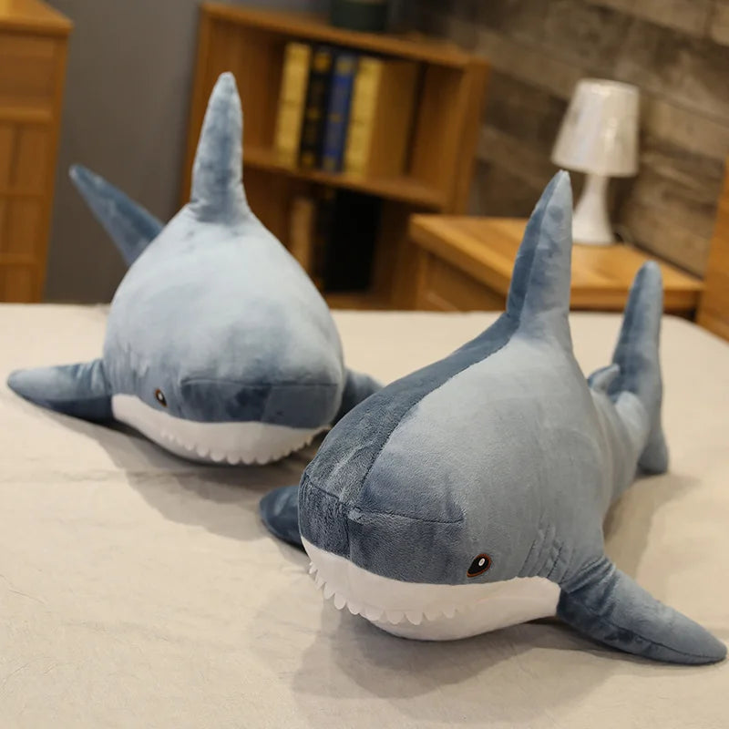 Two plush shark kawaii toys on a bed with a blurred room background