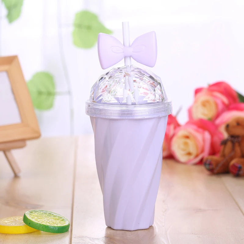Clear kawaii cup with a purple lid and straw featuring a bow design, placed on a wooden surface with flowers and a teddy bear in the background.