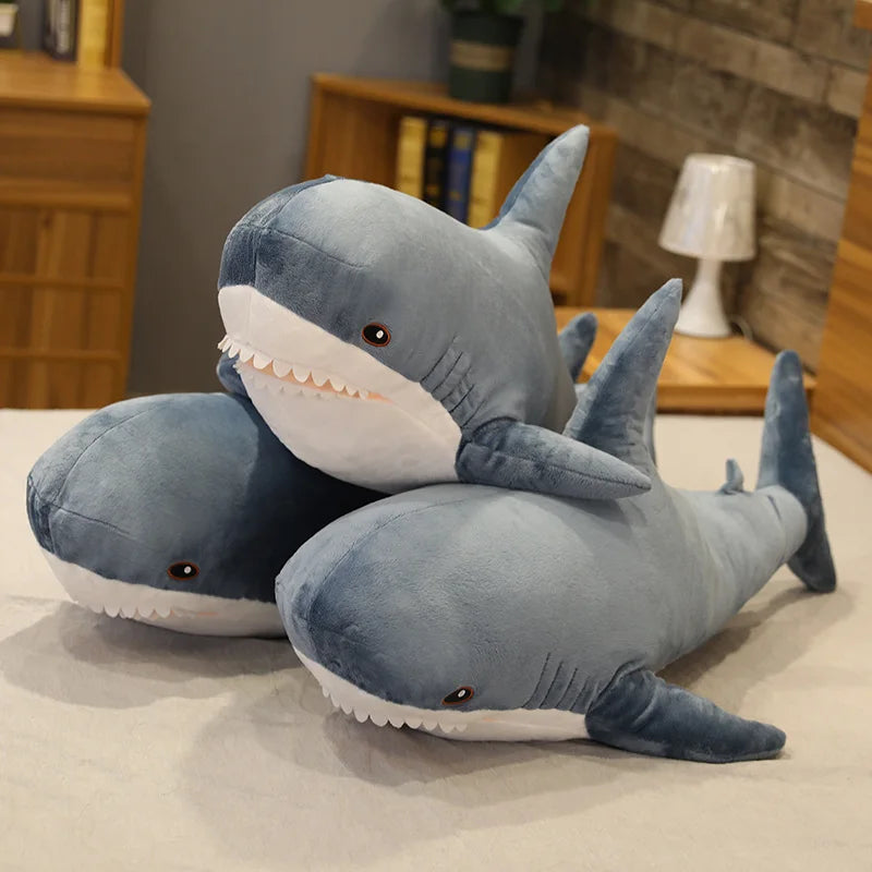 Two large blue shark kawaii plush toys on a light-colored surface with a blurred indoor background.