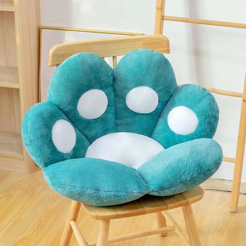 Teal paw-shaped kawaii cushion with white pads on a wooden chair.