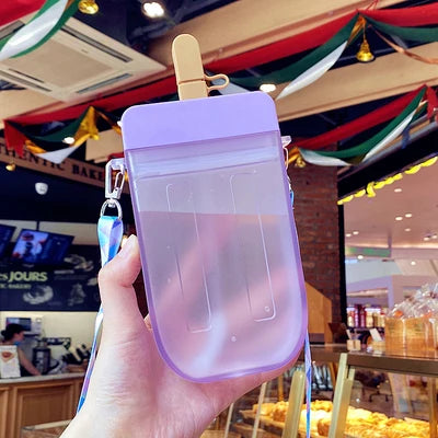 Hand holding a purple popsicle-shaped kawaii water bottle with a blurred indoor background