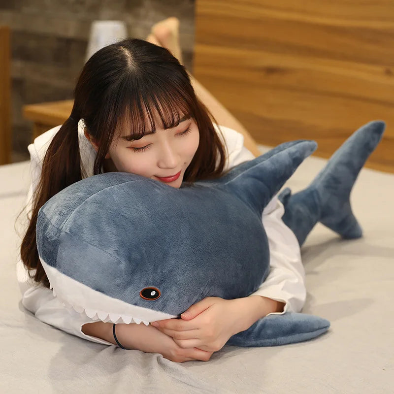 Woman holding a large shark-shaped kawaii pillow on a bed