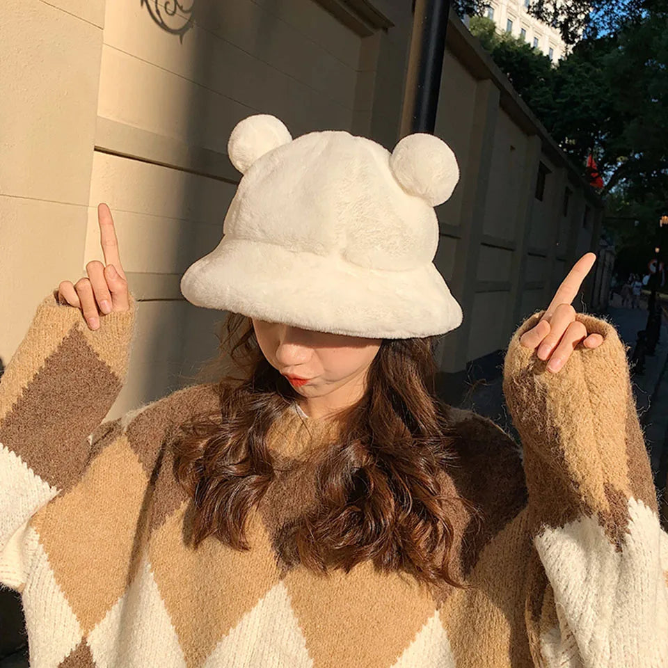 Person wearing a Kawaii white fluffy hat with two pom-poms, standing outdoors.