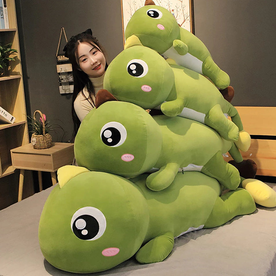 Stack of green kawaii plush caterpillars with a person sitting behind them on a bed.