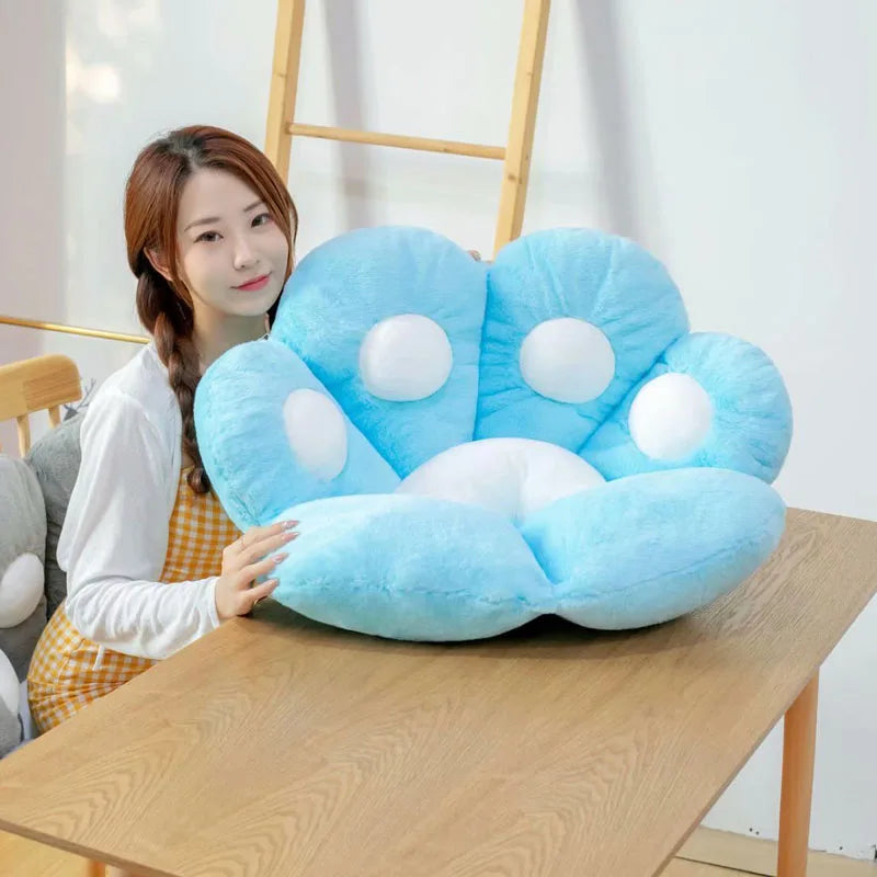 Person holding a large blue paw-shaped kawaii pillow on a wooden table.
