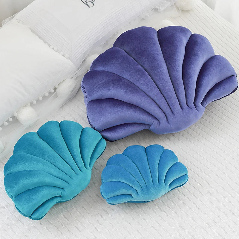 Three shell-shaped kawaii cushions in purple and blue on a textured white surface
