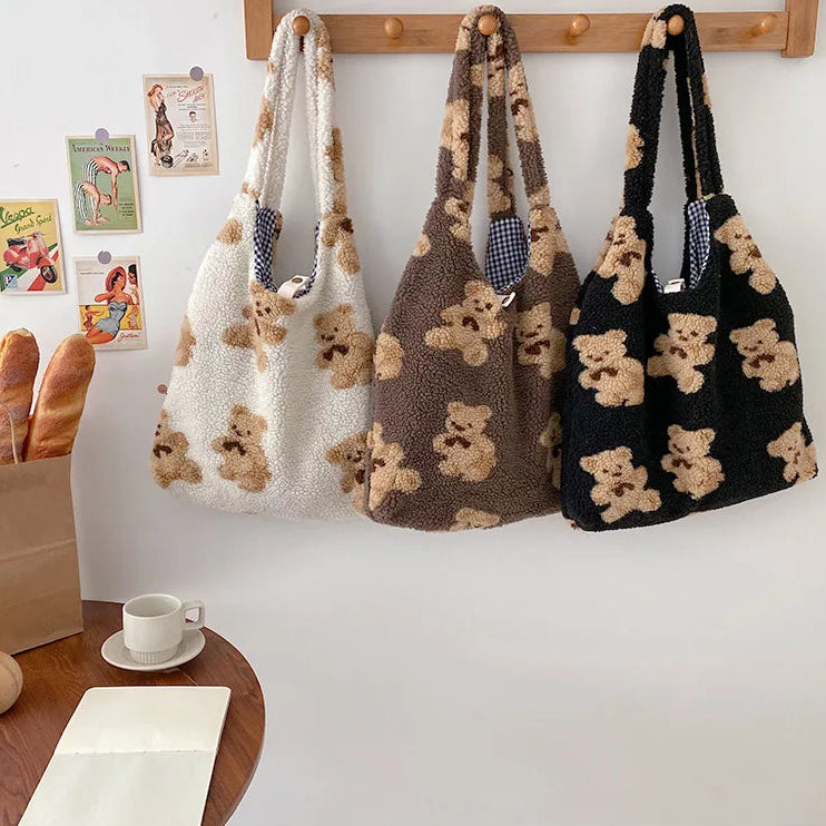 Three knitted bags with kawaii teddy bear patterns hanging on a wooden rack against a white wall.