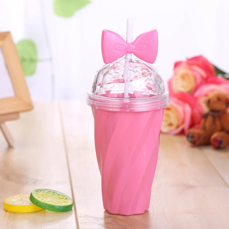 Pink kawaii tumbler with a bow on top on a wooden surface with flowers and a teddy bear in the background.